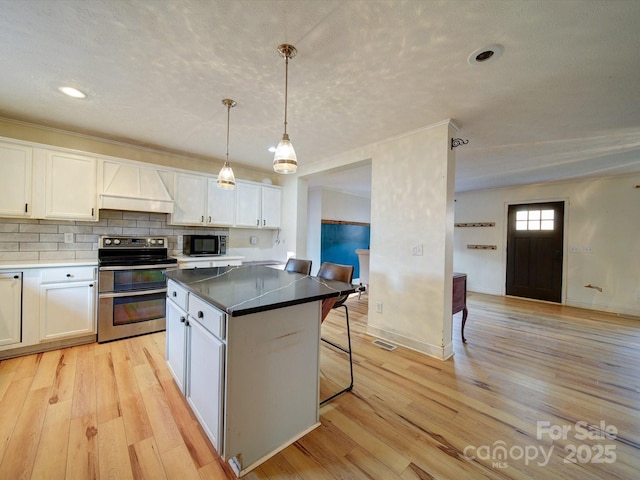 kitchen featuring premium range hood, white cabinetry, hanging light fixtures, double oven range, and a kitchen breakfast bar