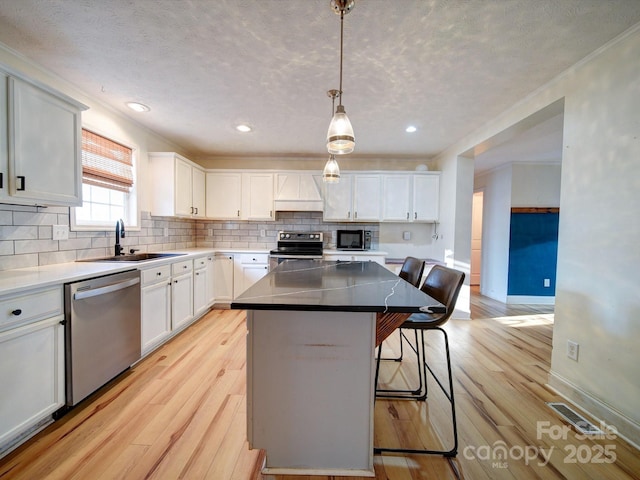 kitchen with a kitchen island, appliances with stainless steel finishes, a breakfast bar, white cabinetry, and hanging light fixtures