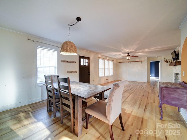 dining room featuring ceiling fan, ornamental molding, a fireplace, and light hardwood / wood-style floors