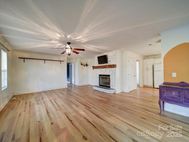 unfurnished living room with ceiling fan, a stone fireplace, a textured ceiling, and light wood-type flooring