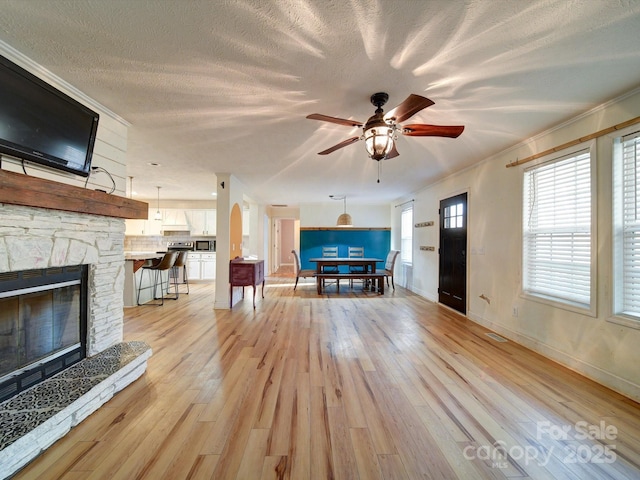 unfurnished living room featuring ceiling fan, a stone fireplace, light hardwood / wood-style flooring, and a textured ceiling