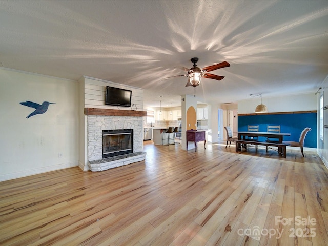 unfurnished living room with ceiling fan, a stone fireplace, a textured ceiling, and light hardwood / wood-style floors