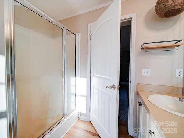 bathroom with hardwood / wood-style flooring, ornamental molding, vanity, and a shower with shower door