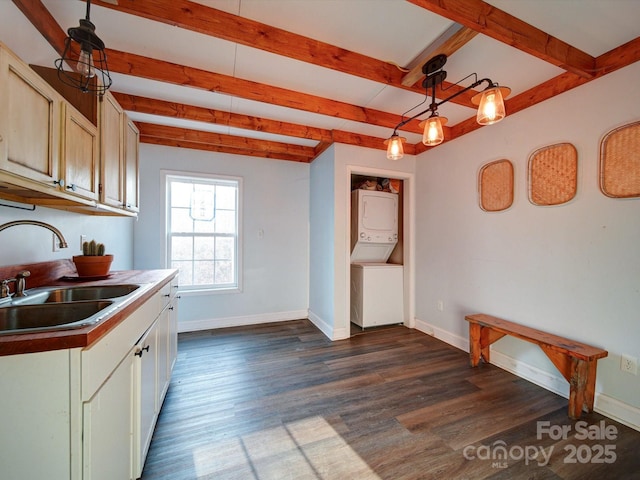 kitchen with dark wood-type flooring, stacked washer / drying machine, sink, hanging light fixtures, and beamed ceiling