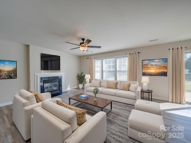 living area with a glass covered fireplace, visible vents, wood finished floors, and a ceiling fan