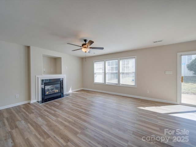 unfurnished living room featuring baseboards, visible vents, ceiling fan, a glass covered fireplace, and light wood-type flooring