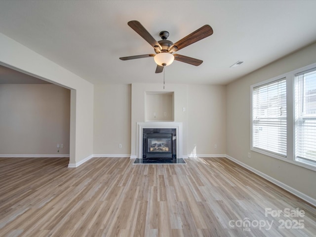 unfurnished living room featuring light wood-type flooring, visible vents, a fireplace with flush hearth, and baseboards