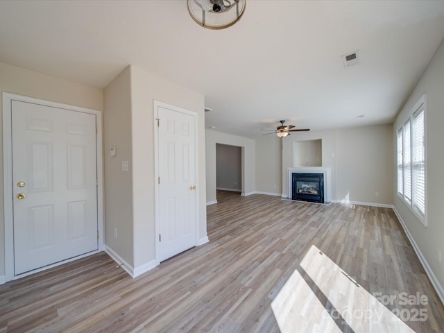 unfurnished living room featuring visible vents, ceiling fan, baseboards, light wood-type flooring, and a glass covered fireplace