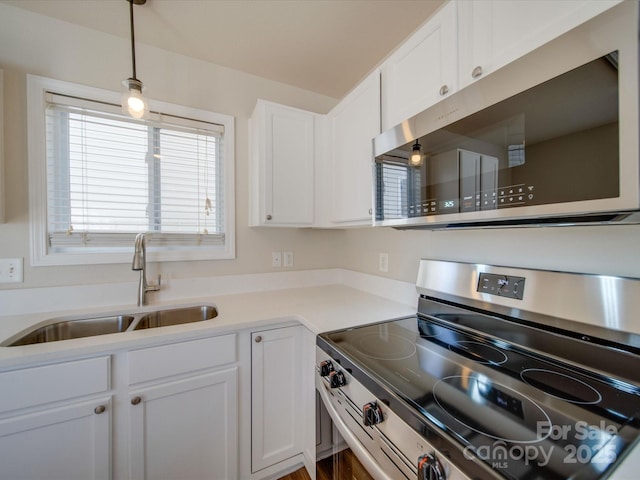 kitchen featuring light countertops, appliances with stainless steel finishes, hanging light fixtures, white cabinetry, and a sink