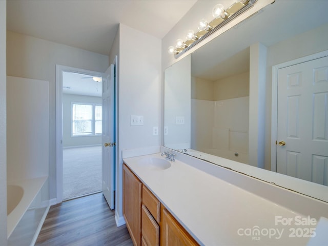 bathroom featuring vanity, a bath, wood finished floors, and baseboards