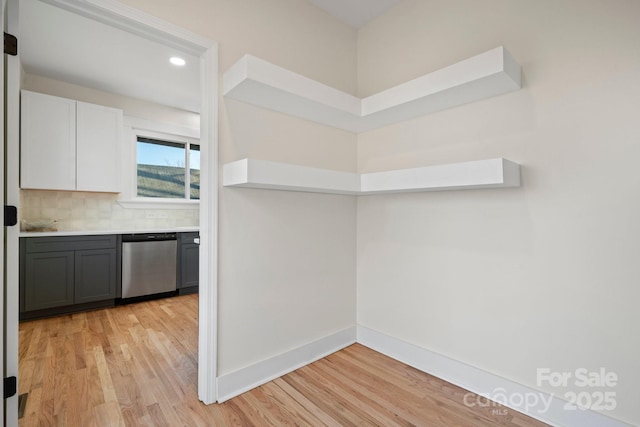 kitchen featuring gray cabinetry, white cabinetry, tasteful backsplash, stainless steel dishwasher, and light hardwood / wood-style floors