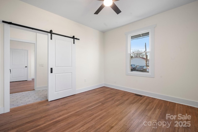 unfurnished room featuring ceiling fan, a barn door, and hardwood / wood-style floors