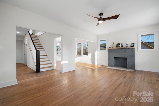 unfurnished living room featuring a ceiling fan, wood finished floors, stairway, and baseboards