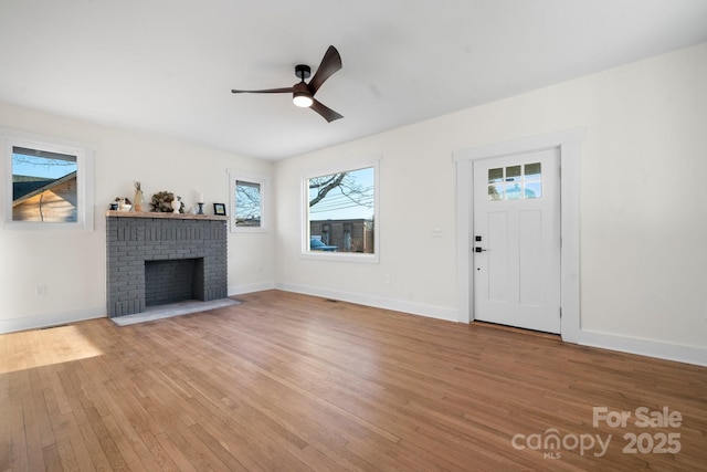 unfurnished living room with wood finished floors, ceiling fan, baseboards, and a brick fireplace