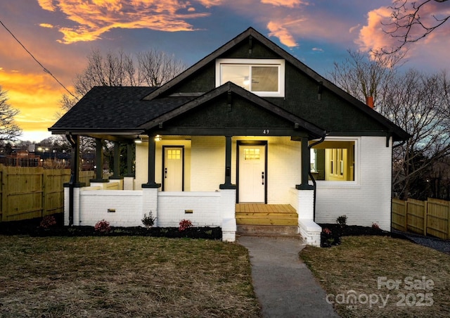 bungalow with covered porch, a shingled roof, and brick siding