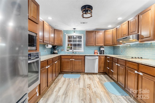 kitchen featuring stainless steel appliances, light stone countertops, visible vents, brown cabinets, and under cabinet range hood