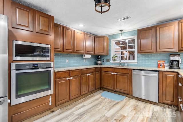 kitchen with stainless steel appliances, light stone countertops, visible vents, a sink, and brown cabinets