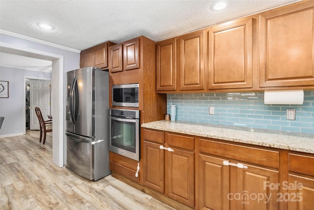 kitchen with tasteful backsplash, appliances with stainless steel finishes, brown cabinets, light stone countertops, and light wood-style floors