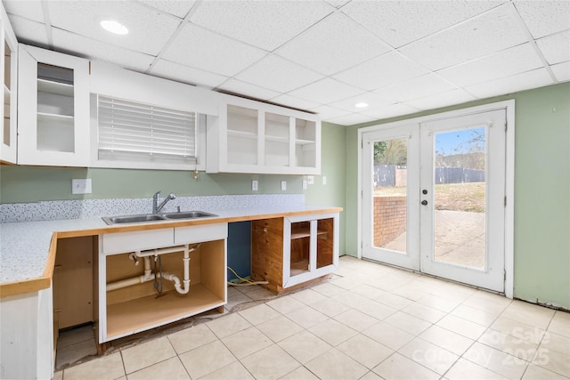 kitchen with a sink, light countertops, a paneled ceiling, and glass insert cabinets