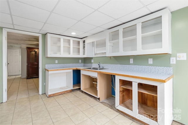 kitchen with light tile patterned floors, a drop ceiling, glass insert cabinets, light countertops, and a sink