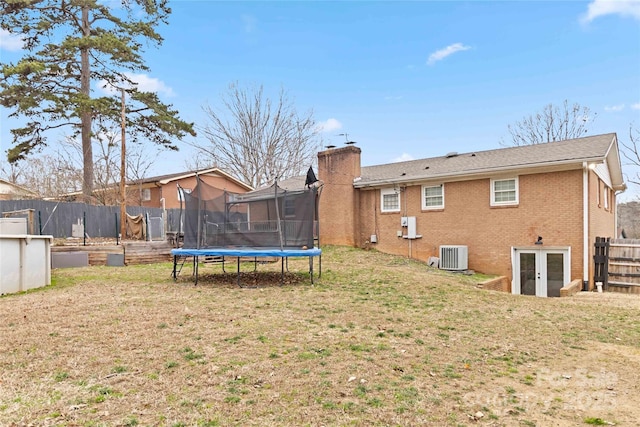 back of property featuring fence, brick siding, a chimney, a trampoline, and a yard