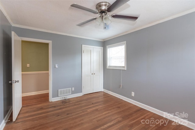 unfurnished bedroom featuring baseboards, visible vents, ornamental molding, dark wood-type flooring, and a closet