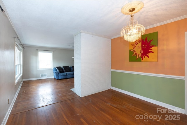 spare room featuring dark wood-style flooring, a notable chandelier, visible vents, ornamental molding, and baseboards