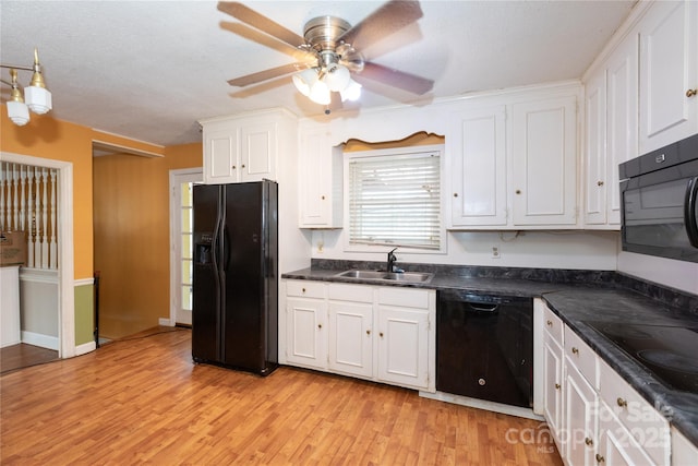 kitchen with a sink, white cabinets, light wood-type flooring, black appliances, and dark countertops