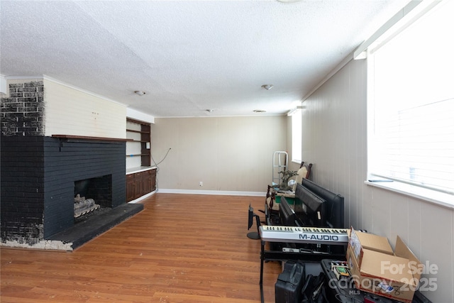 living room with a brick fireplace, a textured ceiling, baseboards, and wood finished floors