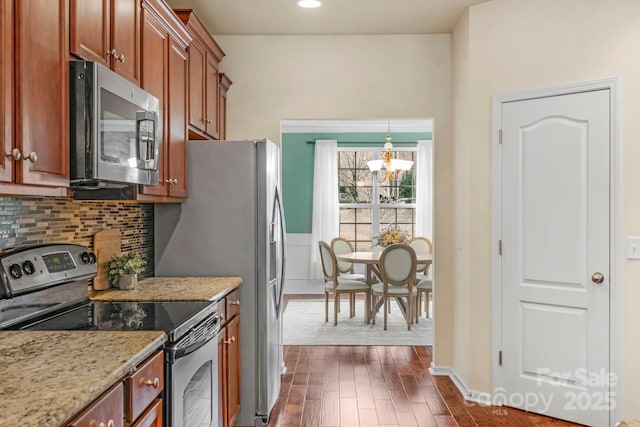 kitchen featuring pendant lighting, dark wood-type flooring, backsplash, stainless steel appliances, and light stone countertops