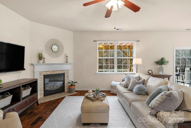 living room with a stone fireplace, a wealth of natural light, ceiling fan, and light wood-type flooring