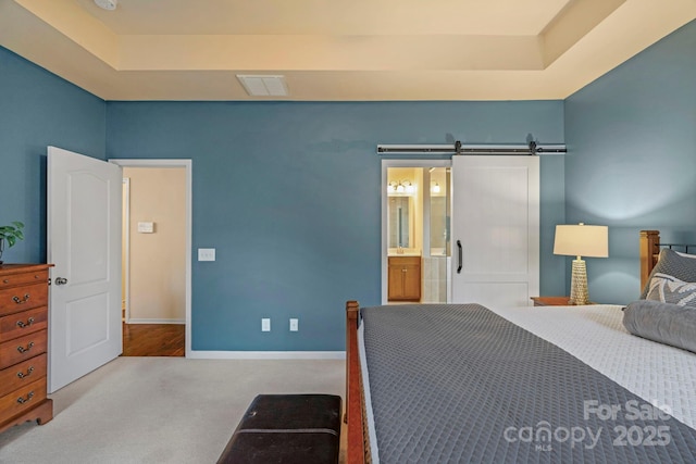 bedroom with ensuite bathroom, a barn door, a raised ceiling, and light carpet