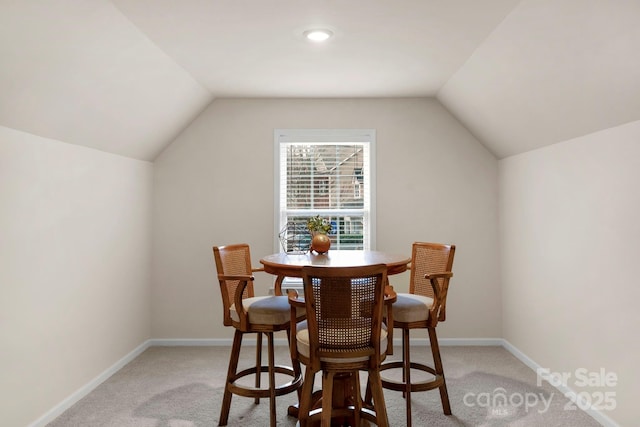 carpeted dining space with vaulted ceiling