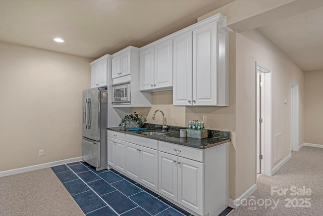 kitchen with appliances with stainless steel finishes, white cabinetry, sink, dark stone countertops, and dark carpet