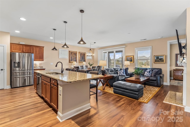 kitchen featuring sink, appliances with stainless steel finishes, hanging light fixtures, light stone countertops, and an island with sink