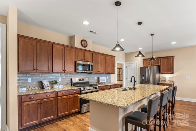 kitchen with sink, appliances with stainless steel finishes, hanging light fixtures, a center island with sink, and a kitchen bar