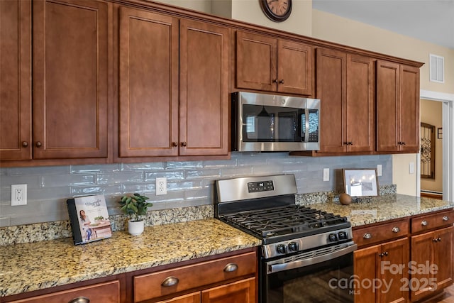 kitchen with stainless steel appliances, tasteful backsplash, and light stone counters