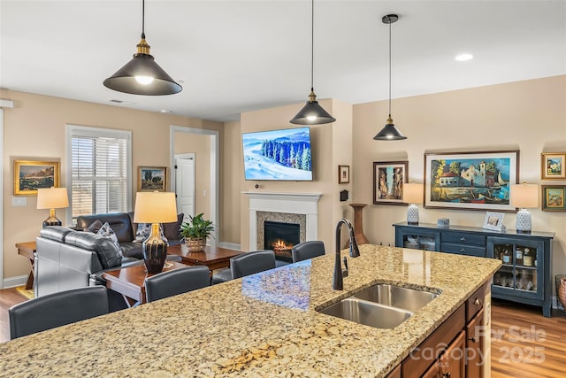 kitchen with light stone countertops, sink, hanging light fixtures, and light wood-type flooring