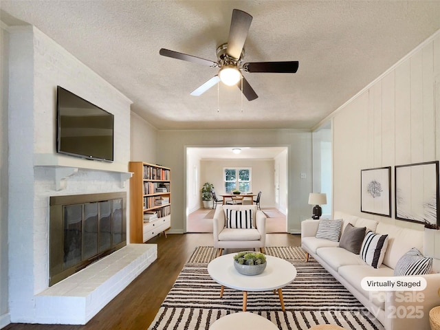 living room with dark hardwood / wood-style floors, a fireplace, ornamental molding, ceiling fan, and a textured ceiling