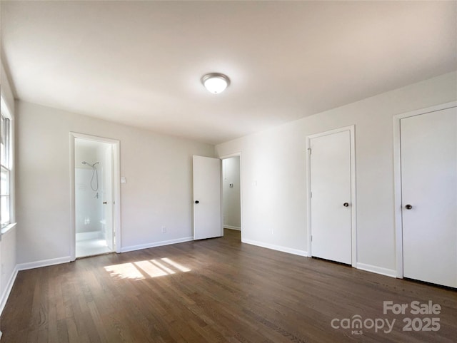 unfurnished bedroom with ensuite bathroom, dark wood-type flooring, and two closets