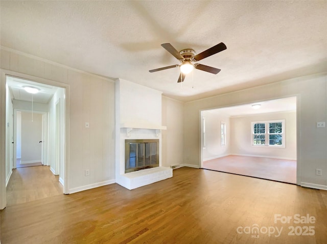 unfurnished living room with ceiling fan, a fireplace, hardwood / wood-style floors, and a textured ceiling