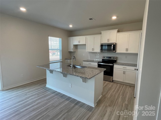 kitchen featuring a kitchen island with sink, sink, stone counters, and appliances with stainless steel finishes