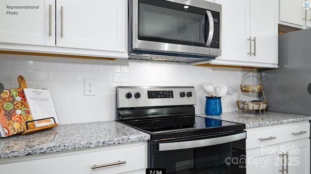 kitchen featuring stainless steel appliances, light stone countertops, white cabinets, and backsplash