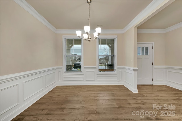 unfurnished dining area featuring an inviting chandelier, crown molding, and light hardwood / wood-style floors