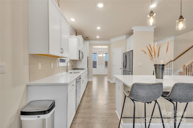 kitchen with decorative light fixtures, light wood-type flooring, appliances with stainless steel finishes, white cabinets, and backsplash