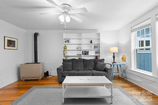 living room with ceiling fan, a wood stove, and light hardwood / wood-style floors