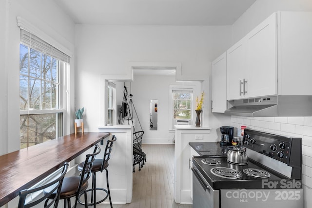 kitchen with tasteful backsplash, white cabinetry, light hardwood / wood-style floors, and stainless steel range with electric stovetop