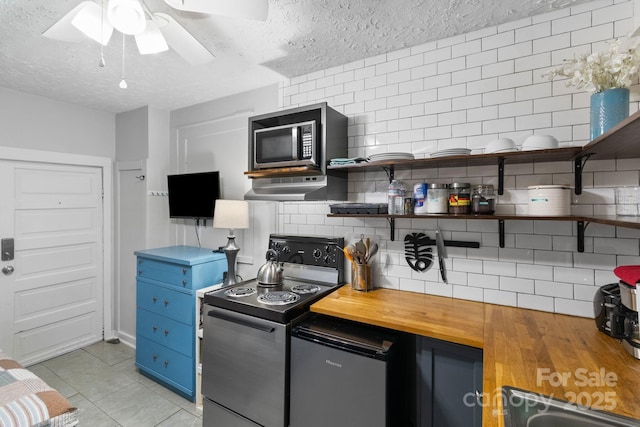kitchen with tasteful backsplash, wooden counters, electric range oven, light tile patterned floors, and a textured ceiling