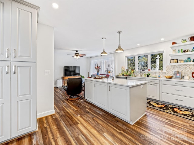 kitchen with tasteful backsplash, an island with sink, white cabinetry, hanging light fixtures, and dark wood-type flooring