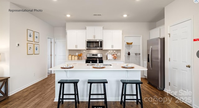 kitchen with sink, backsplash, stainless steel appliances, an island with sink, and white cabinets